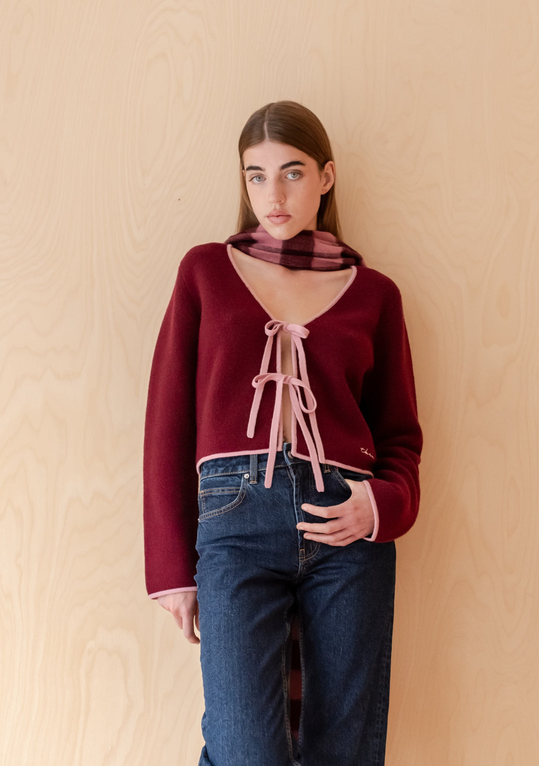 Model wearing TBCo Merino Wool Tie Cardigan in Burgundy, showcasing its adjustable tie closures and V-neck, paired with a matching scarf and high-waisted jeans.