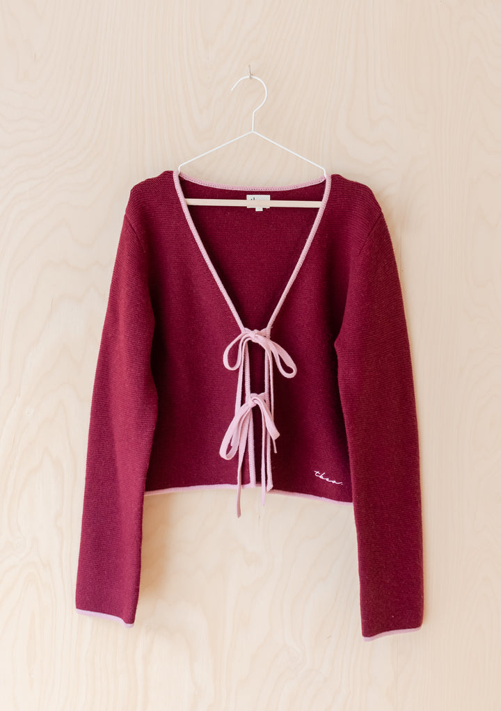 TBCo Merino Wool Tie Cardigan in Burgundy featuring pink trim, V-neck, and tie-bows, crafted from merino wool for versatile autumn layering.
