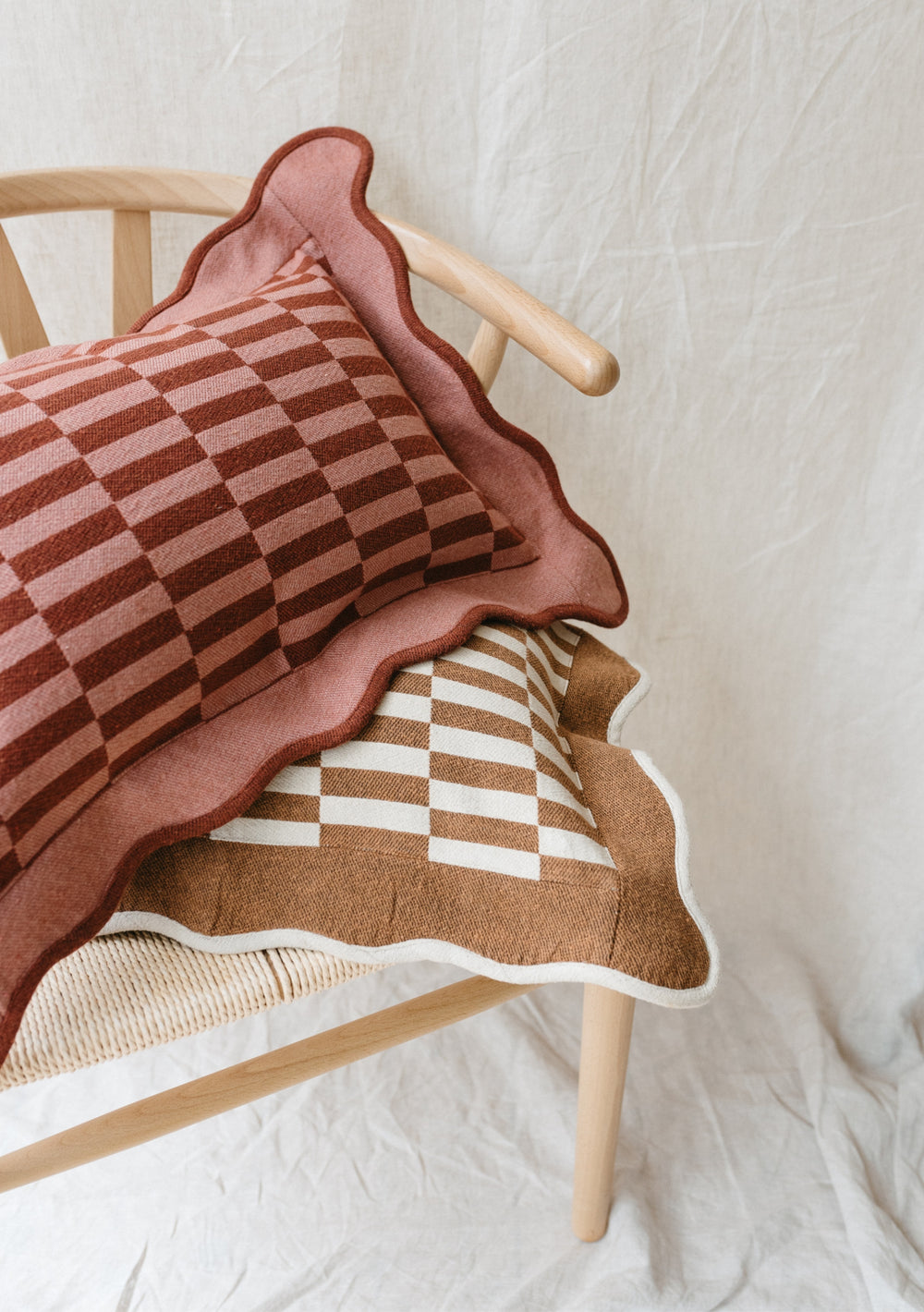 TBCo Cotton Cushion Cover in camel and cream checkerboard pattern with scalloped edges stacked on wooden chair