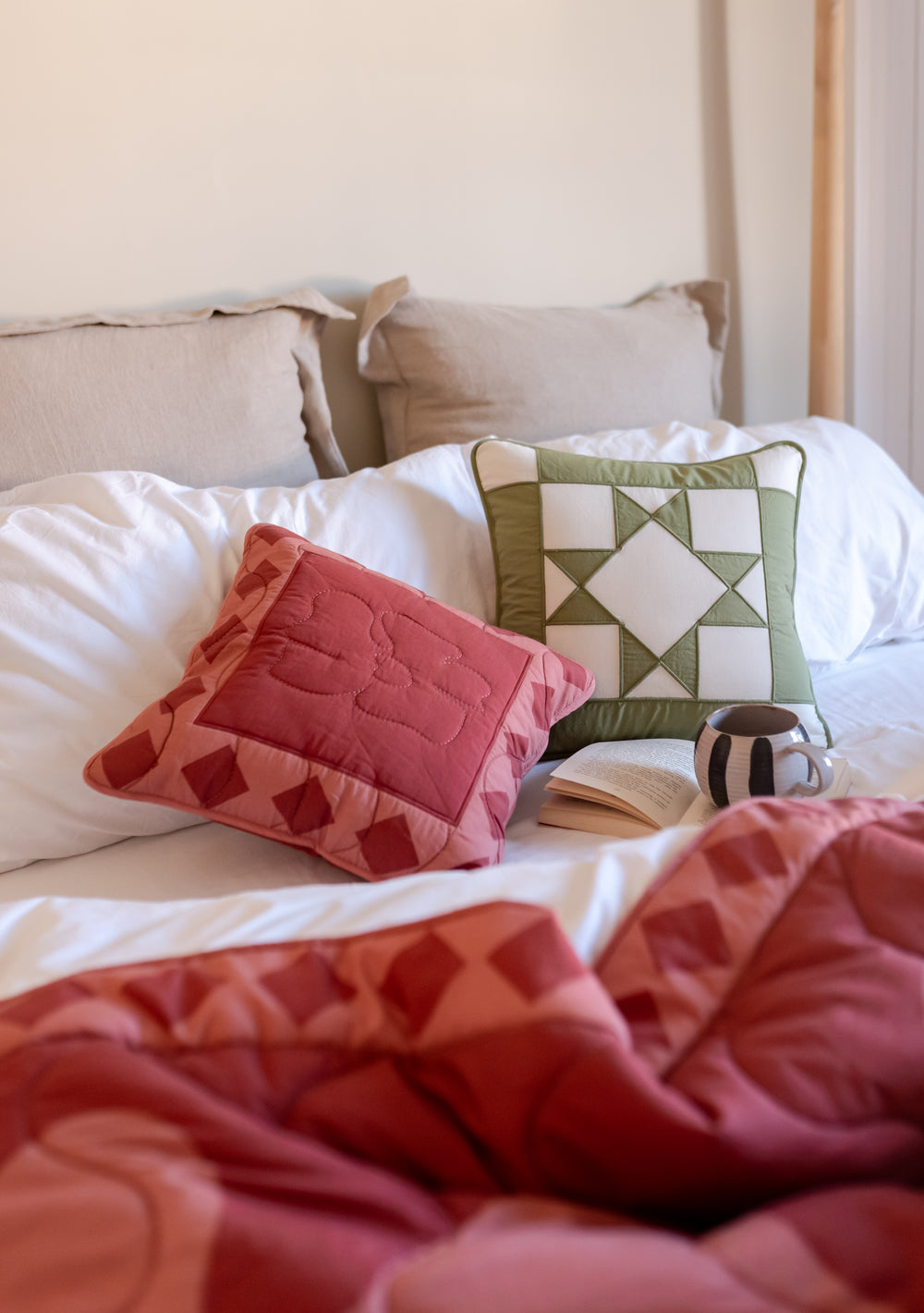 TBCo Quilted Cushion Cover in Flora shown in pink and sage green geometric patterns on cosy white bedding with matching throw