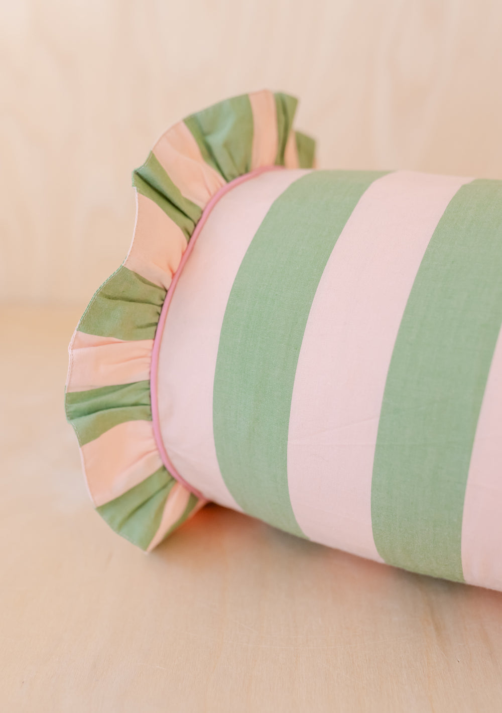 TBCo Cotton Bolster Cushion Cover featuring green and pink stripes with decorative ruffle trim, displayed on light wooden surface