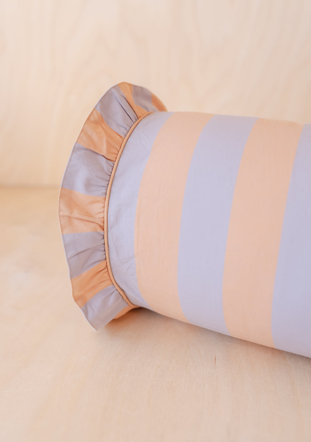 TBCo Cotton Bolster Cushion Cover featuring orange and lilac stripes with ruffle trim, photographed on wooden surface