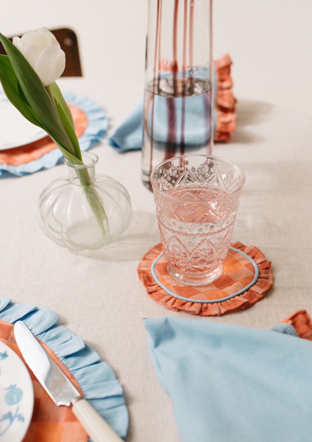 Glass of water on a TBCo Cotton Coasters Set of 2 in Apricot Checkerboard with ruffle and blue piping, portrait view