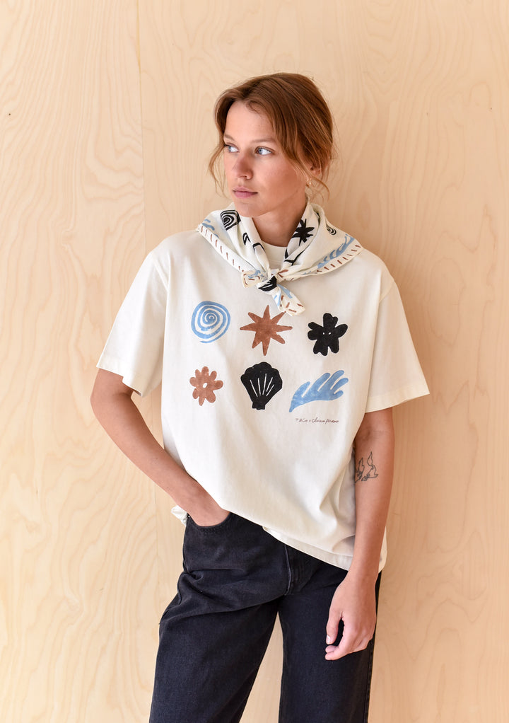 TBCo Chiara Perano Artist Series Cotton Square Triangle Neck Scarf and Cotton T-shirt worn by a model standing in front of a wooden background. 