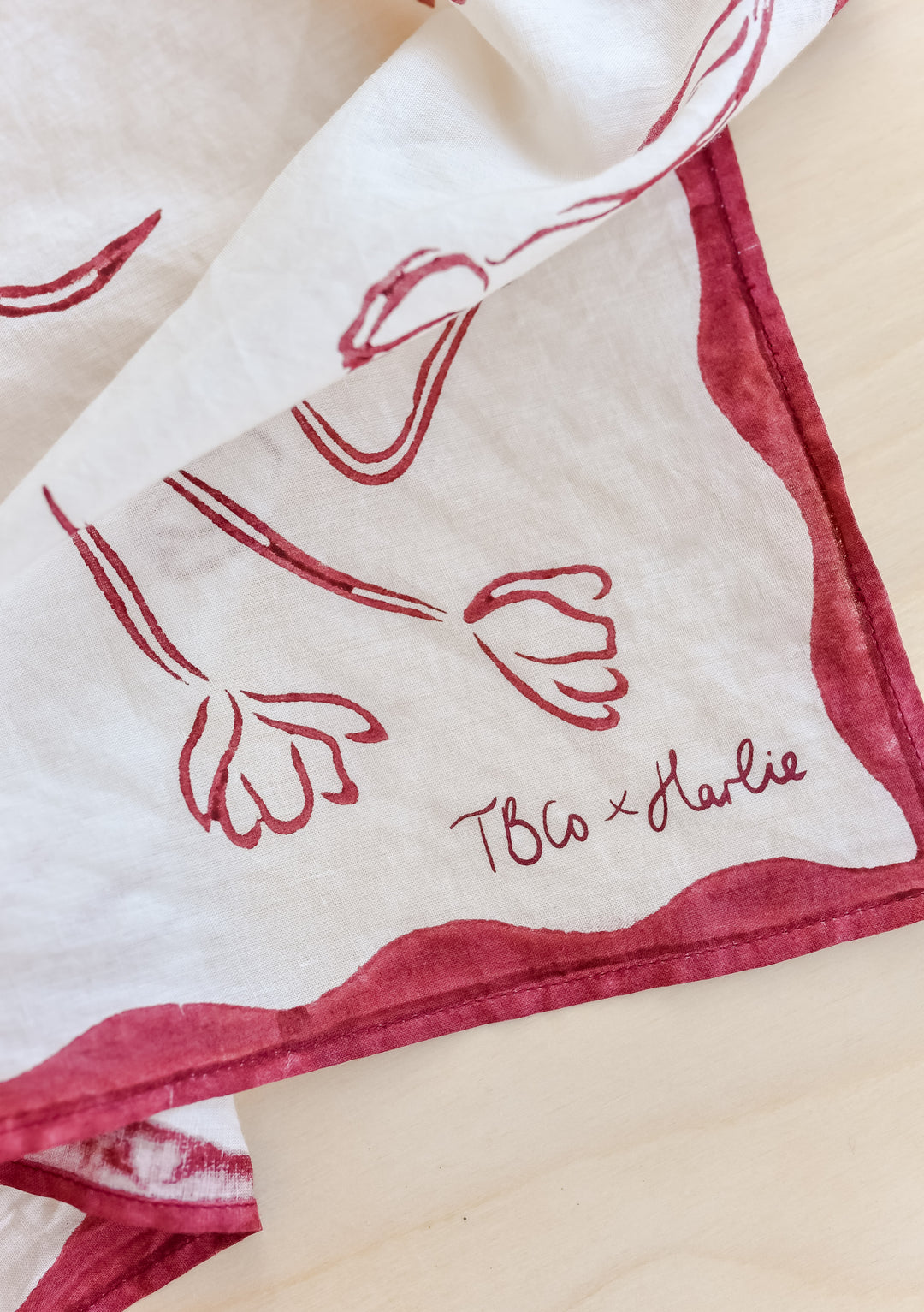 Close-up of TBCo x Harlie Briggs Artist Series cotton triangle neck scarf in white with red floral line art, featuring the TBCo x Harlie logo

