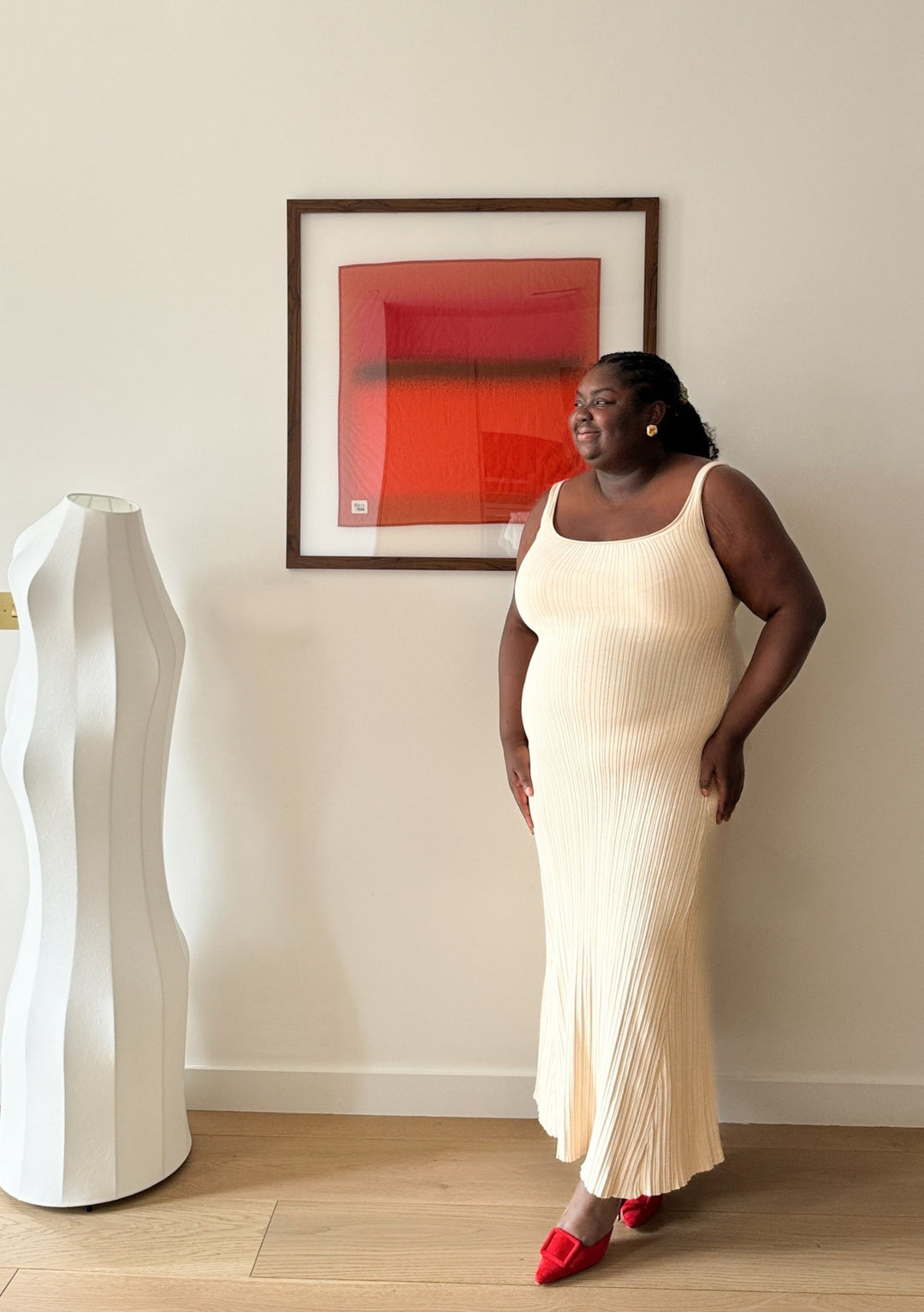Woman wearing a cream dress standing near a framed red scarf from the Sample Sale TBCo x Abisola Omole Hues Cotton Scarf collection