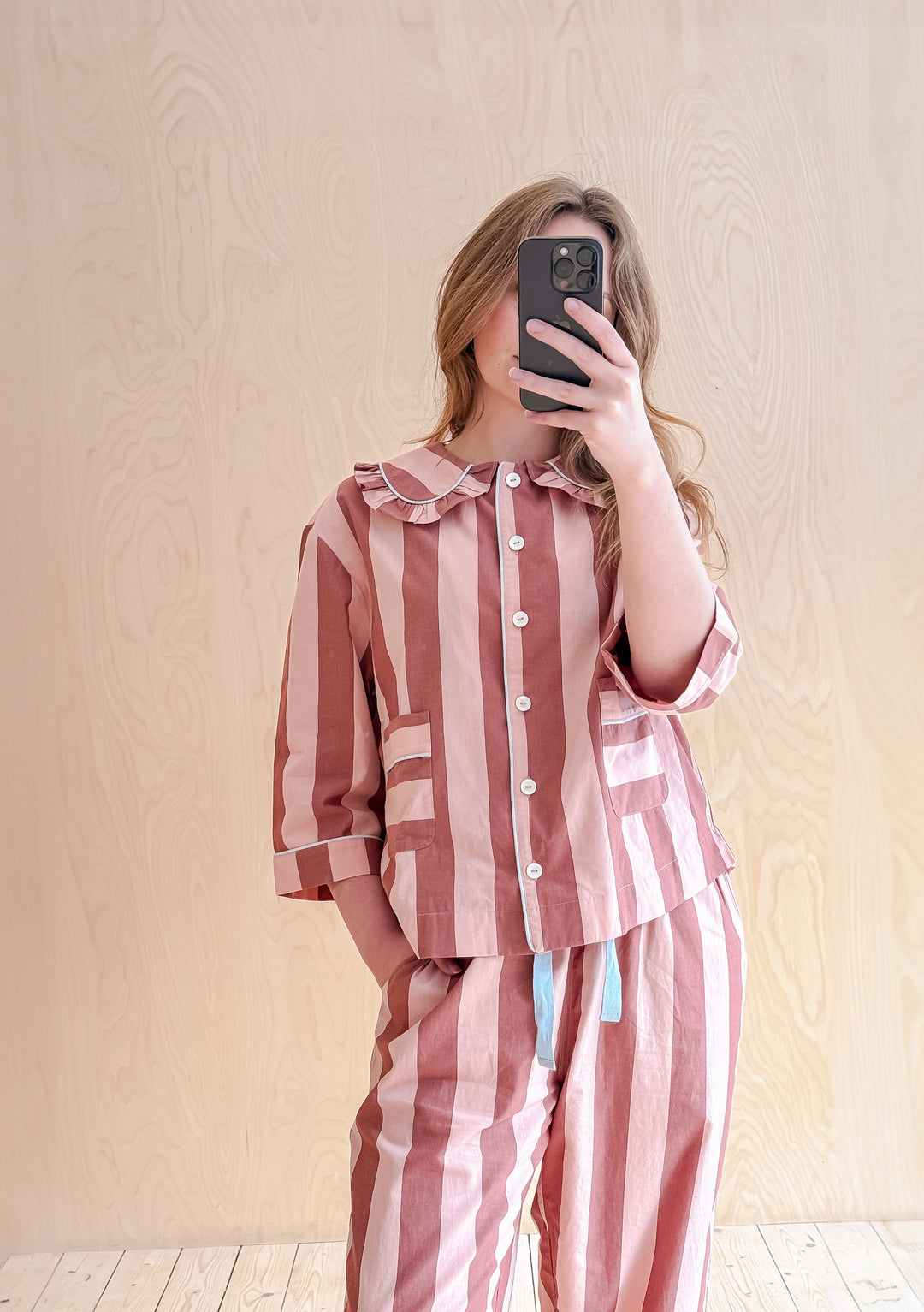 Pink and red striped cotton pyjamas from TBCo featuring ruffle collar and cropped sleeves, shown on wooden background