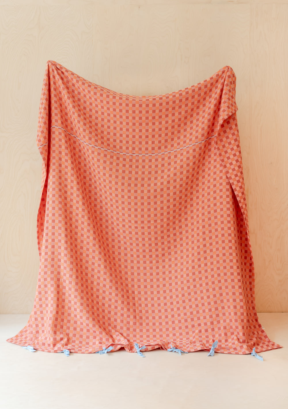 TBCo Cotton Duvet Cover in apricot checkerboard pattern, displayed with blue tie closures against cream wall