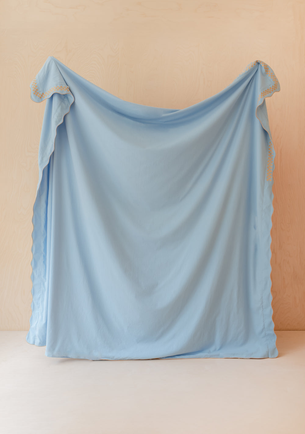 TBCo cotton and linen duvet cover in light blue with camel scalloped embroidery trim, displayed hanging against beige wall