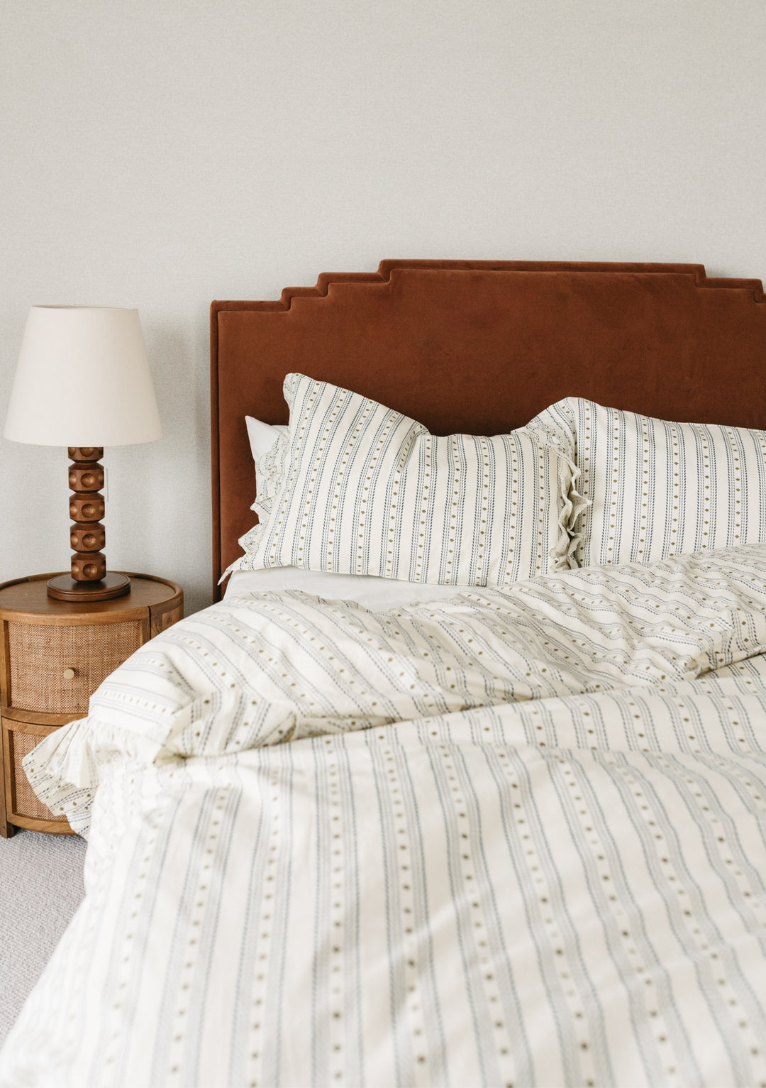 Styled TBCo Cotton Duvet Cover in white and grey stripe pattern, shown on bed with brown velvet headboard and wooden lamp