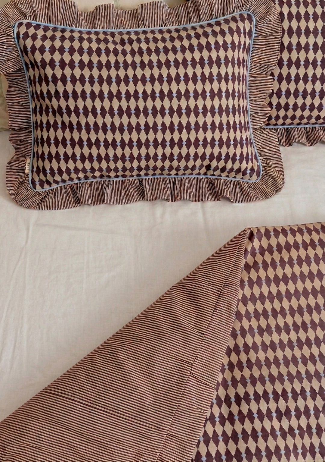 Pair of Cotton Pillowcases in Camel Harlequin by TBCo with diamond pattern and striped ruffle edges on soft bedding