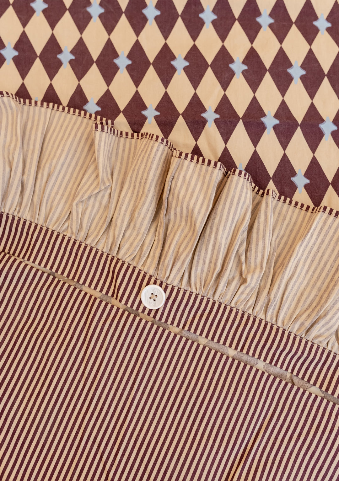 Close-up of TBCo Cotton Duvet Cover in Camel Harlequin showing reversible harlequin and striped patterns with ruffled edge and button closure.