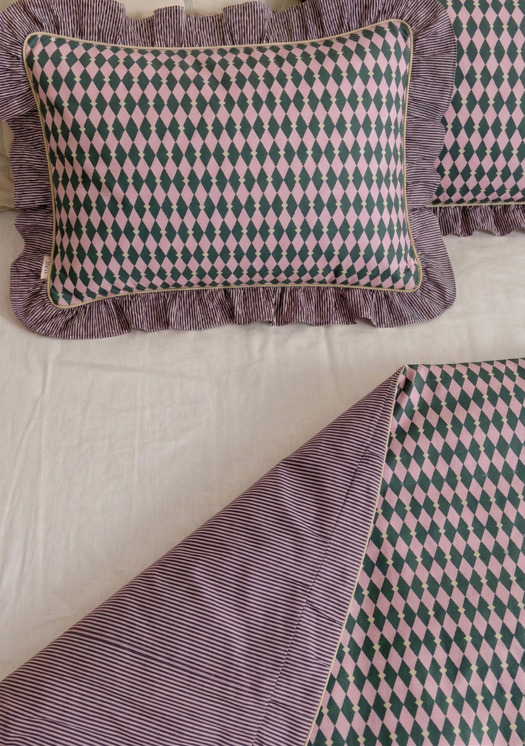 Pair of Cotton Pillowcases in Pink Harlequin by TBCo with pink and green diamond pattern and striped ruffle trim on bed