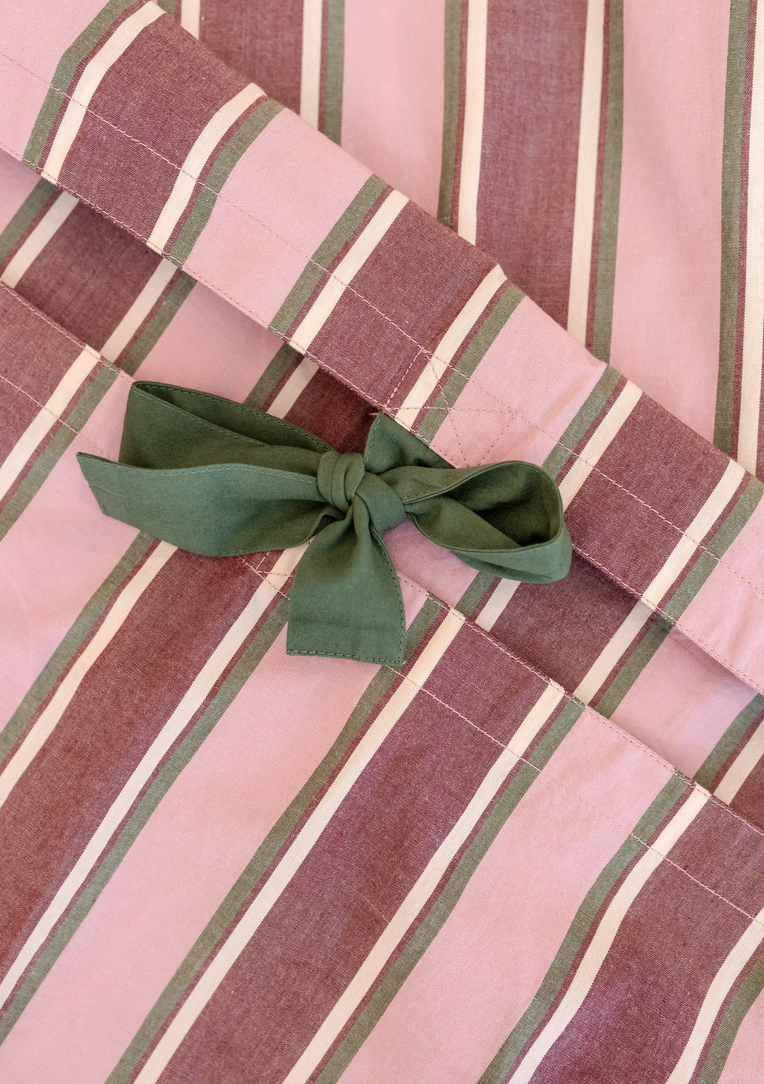 Close-up of pink stripe Cotton Duvet Cover by TBCo featuring green tie closures and breathable cotton poplin fabric.