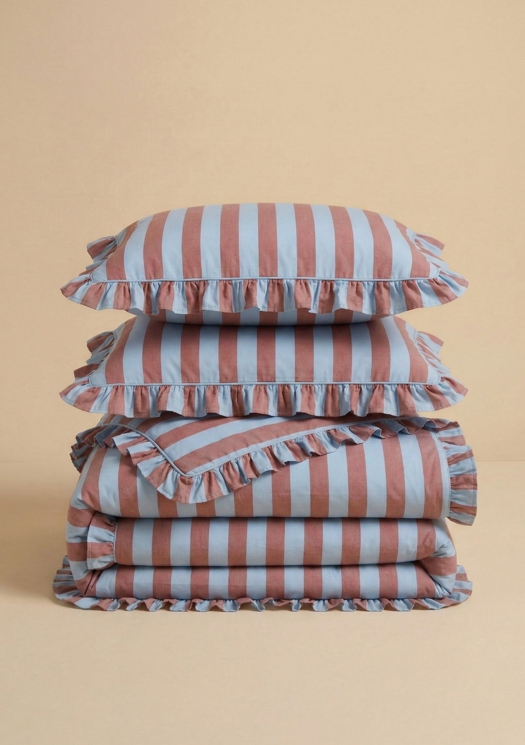 Pair of Cotton Pillowcases in Blue & Red Stripe by TBCo stacked on folded matching cotton bedding with ruffled edges