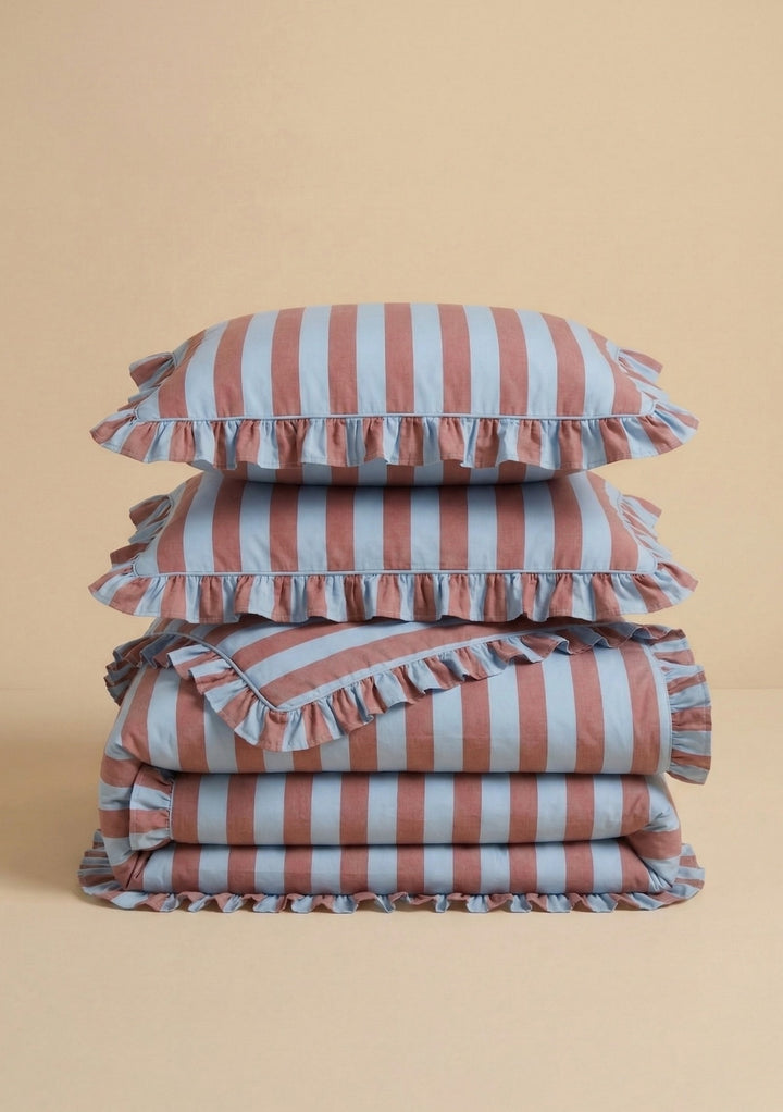 Pair of Cotton Pillowcases in Blue & Red Stripe by TBCo stacked on folded matching cotton bedding with ruffled edges