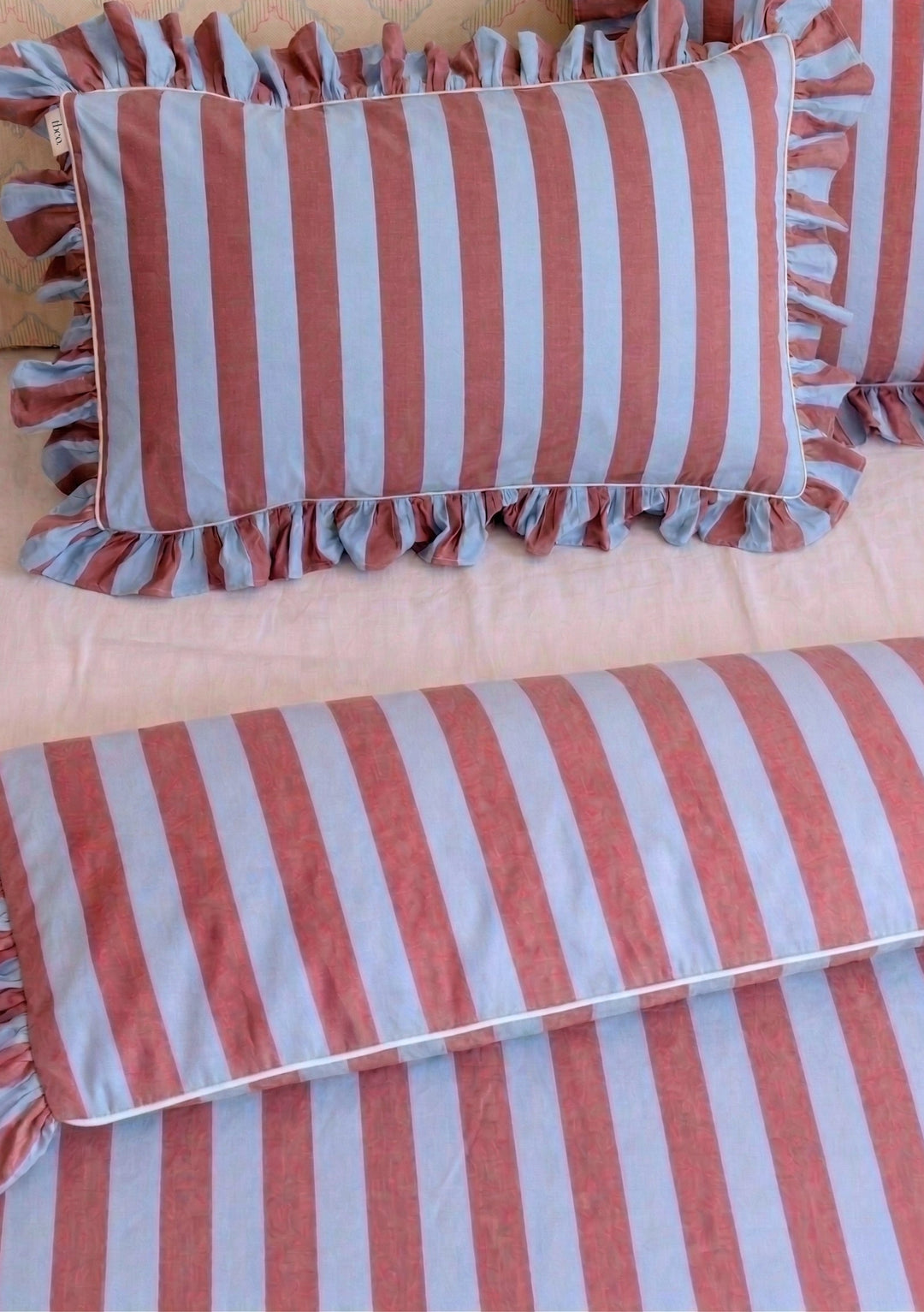 Pair of Cotton Pillowcases in Blue & Red Stripe with ruffled edges by TBCo arranged on soft pastel bedding setting