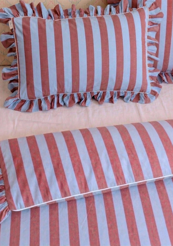 Pair of Cotton Pillowcases in Blue & Red Stripe with ruffled edges by TBCo arranged on soft pastel bedding setting