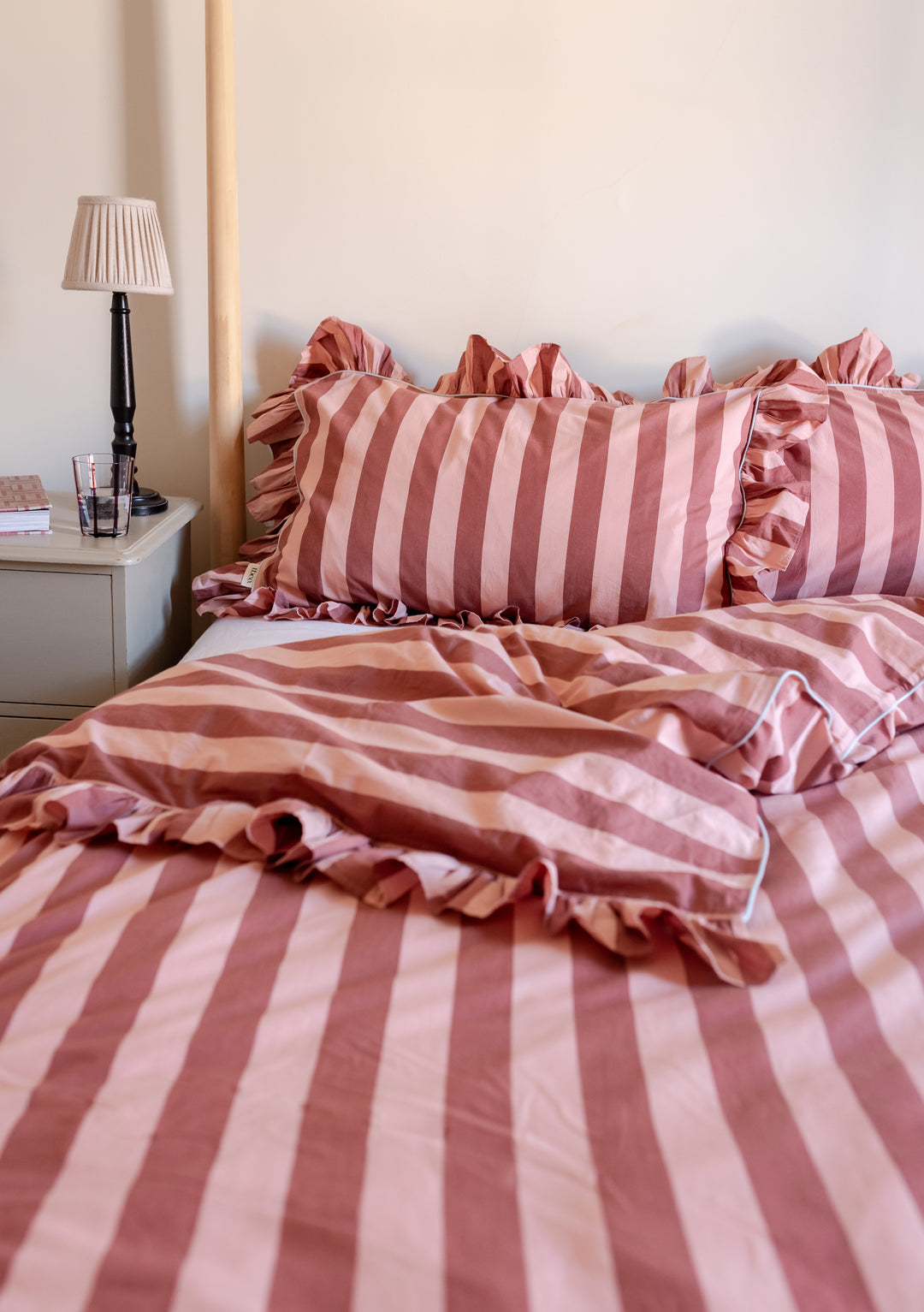 TBCo Cotton Duvet Cover in Pink and Red Stripe with ruffled edges shown on bed with matching pillowcases and bedside lamp