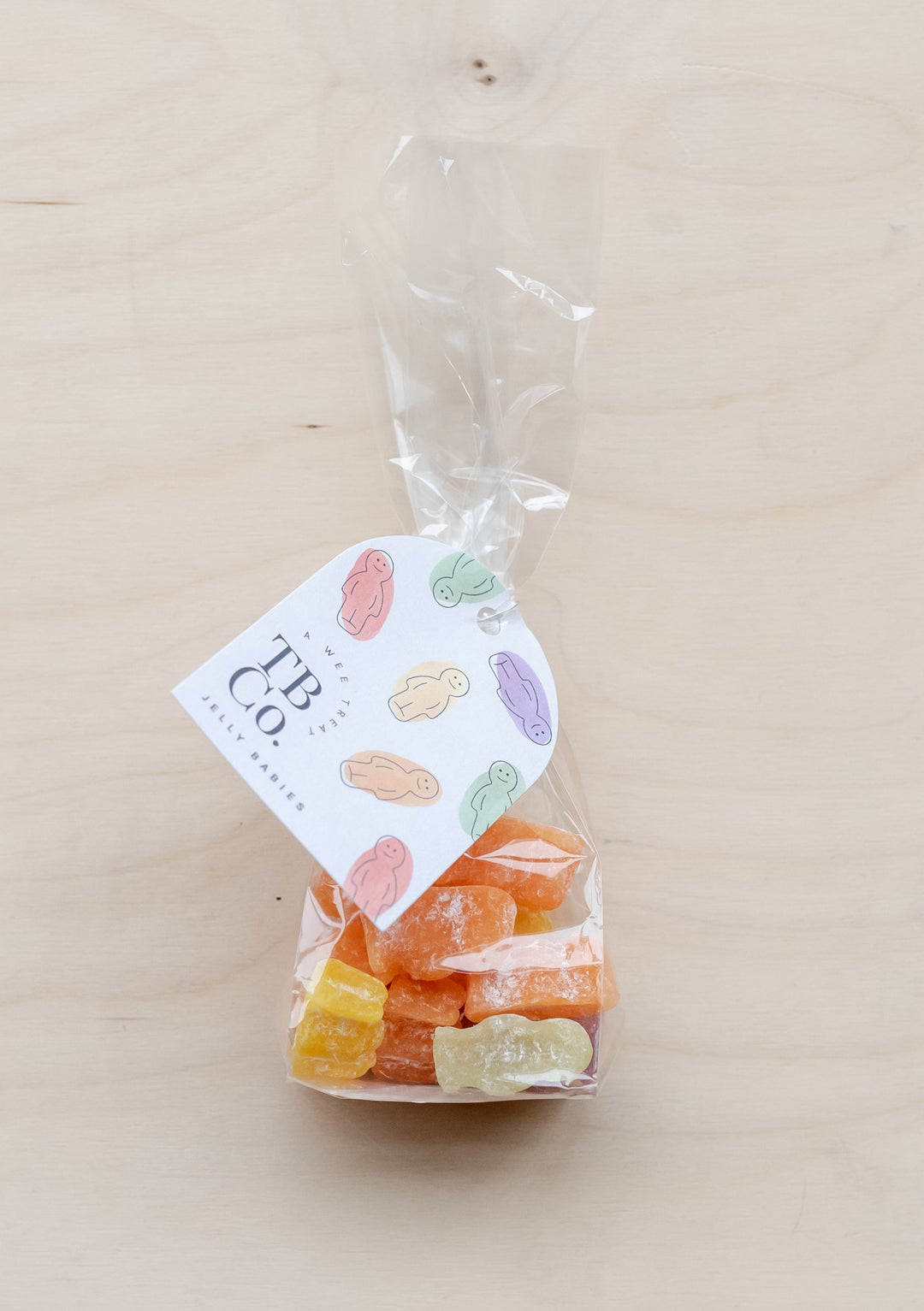 Colourful TBCo Jelly Babies sweets in clear bag with brand tag featuring pastel baby illustrations on wooden surface