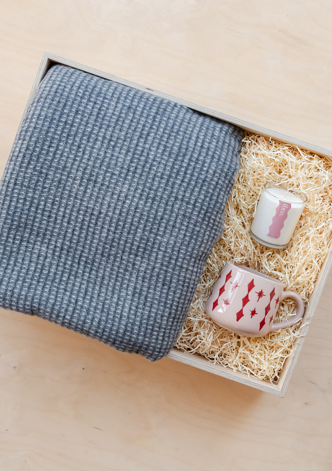 TBCo Ready-Made Holiday Gift Box featuring grey waffle blanket, pink celestial mug and scented candle nestled in straw