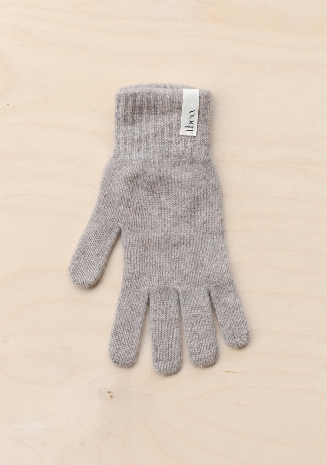 TBCo Cashmere & Merino Gloves in Oatmeal Melange displayed flat on beige surface, showing knitted texture and brand label