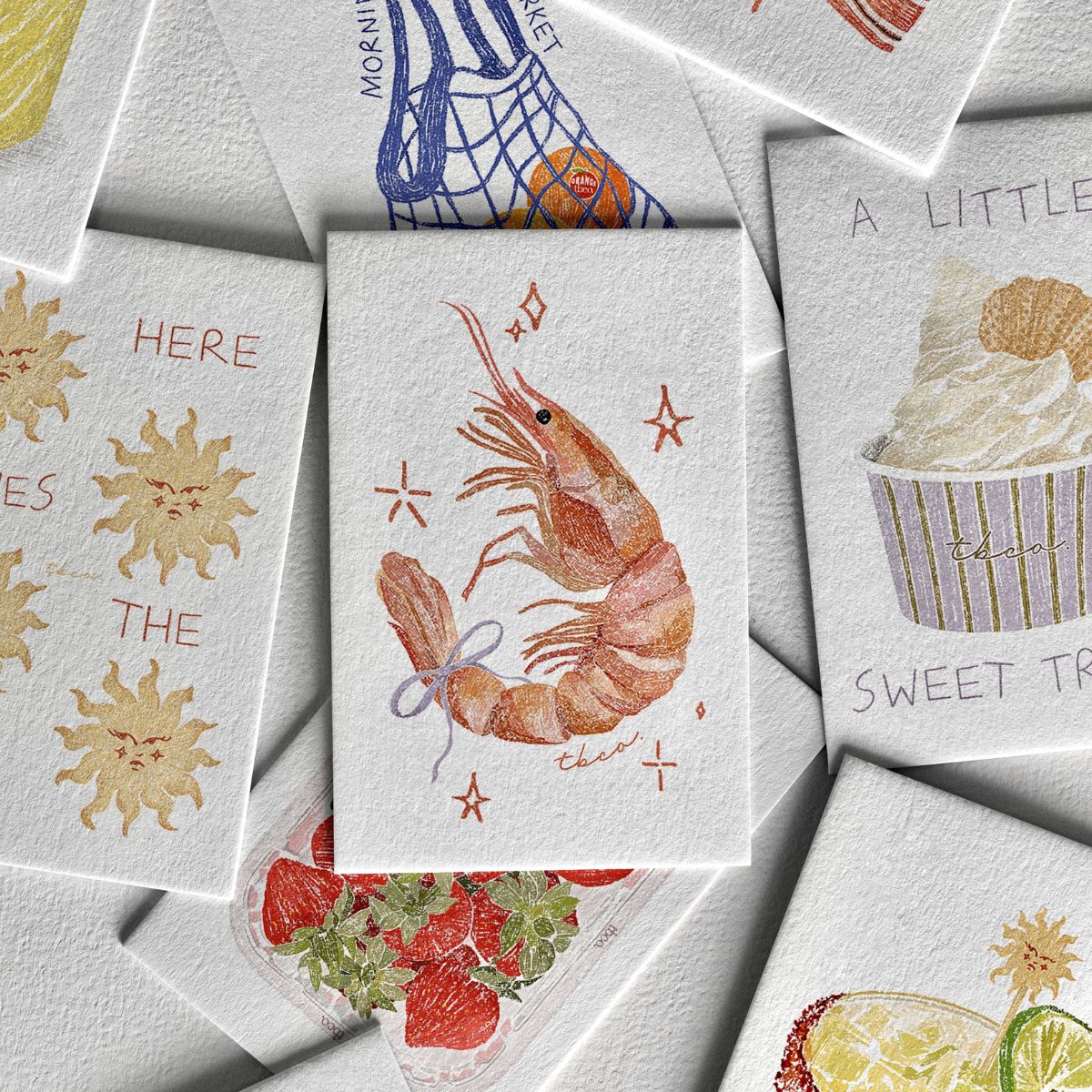 A pile of mini prints featuring illustrations by Eleanor Isobelle Art, featuring TBCo products and motifs including a shrimp with a bow.

