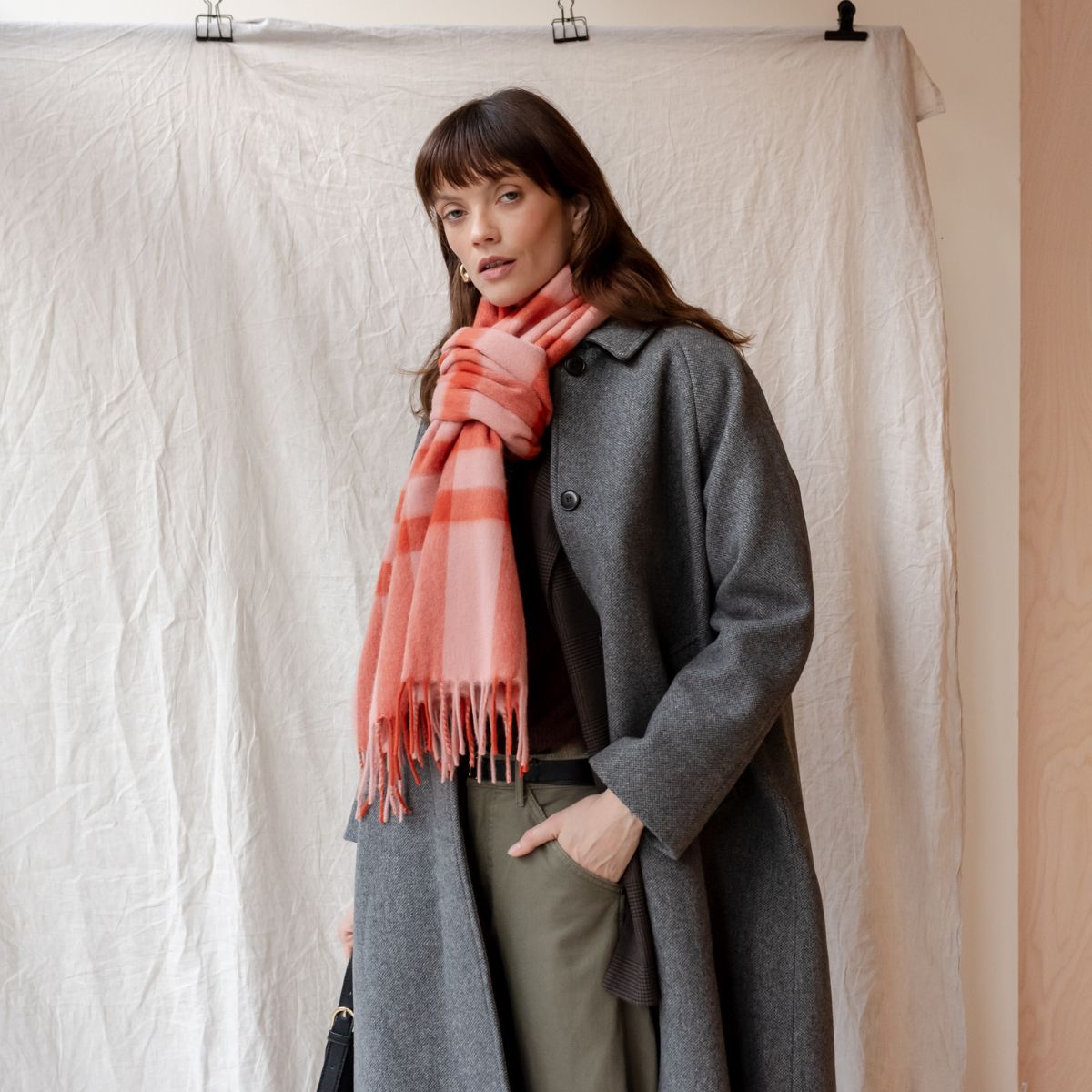 TBCo Lambswool oversized pink check scarf wrapped around the neck, styled with a grey wool coat. A soft and elegant  accessory for timeless layering