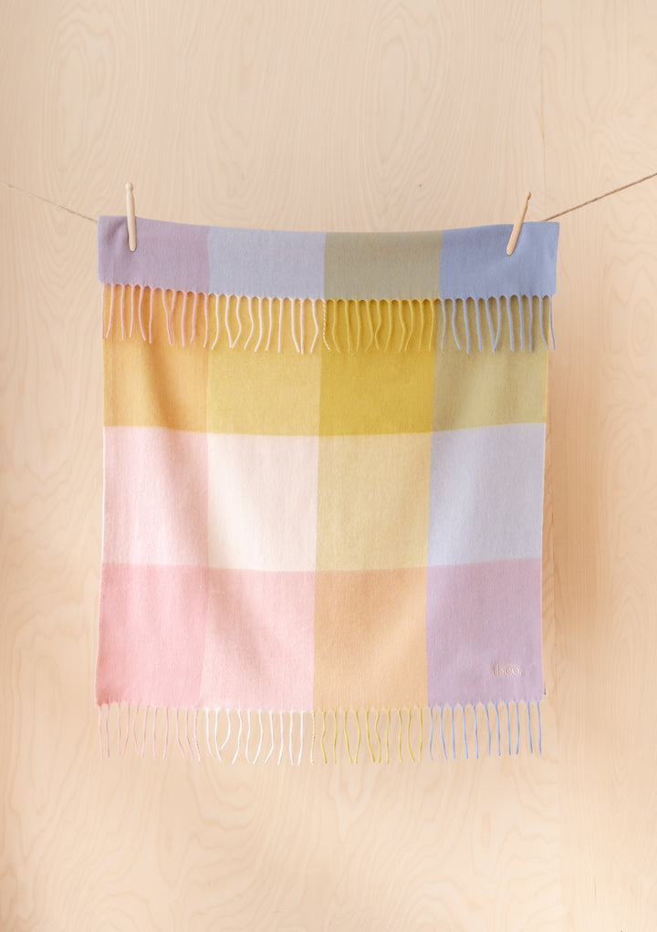 Lambswool Baby Blanket in Pink Block Check by TBCo hanging on a line with fringed edges in portrait view