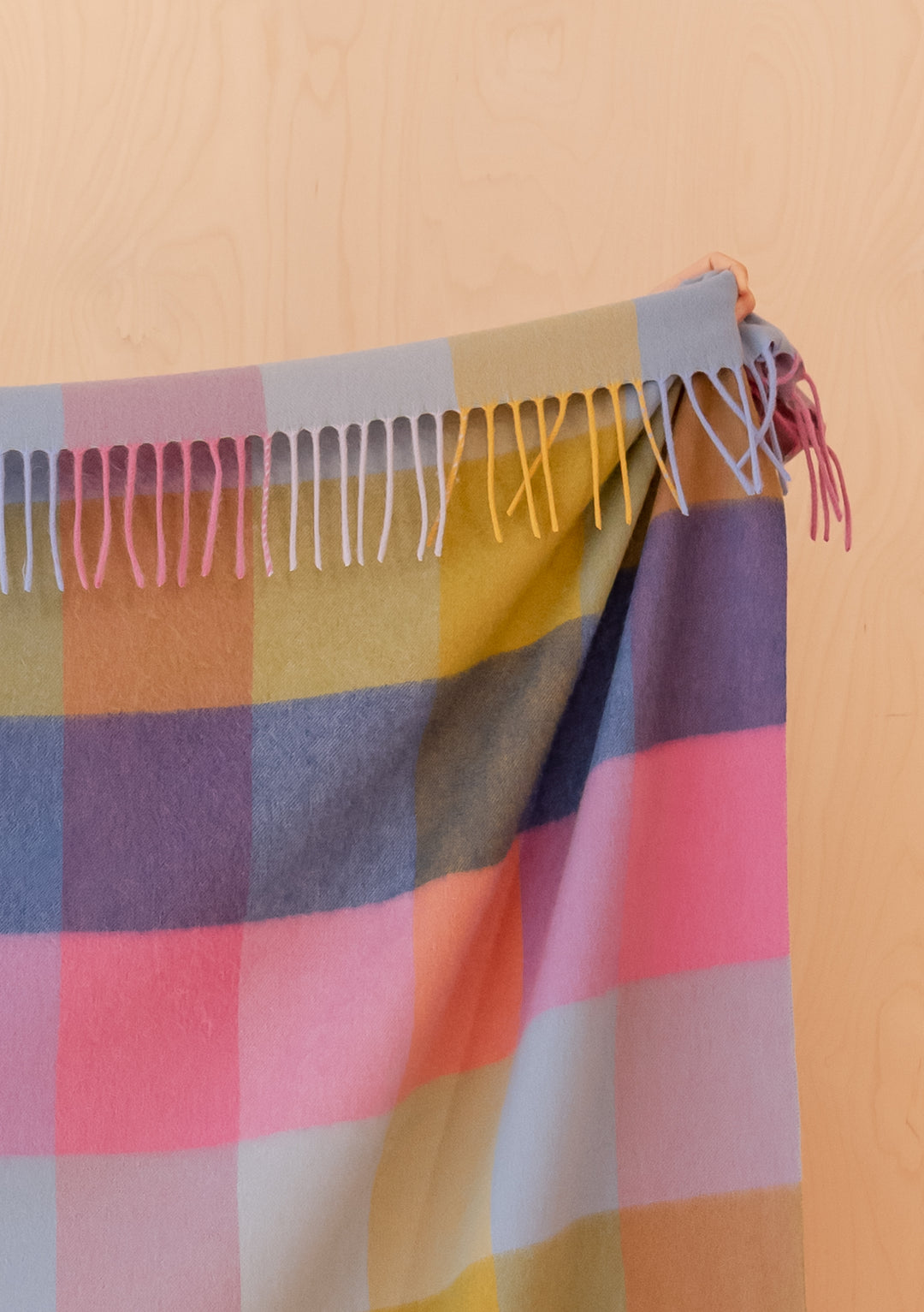Portrait image of TBCo Lambswool Blanket in Pink Block Check with fringed edges draped against light wood background