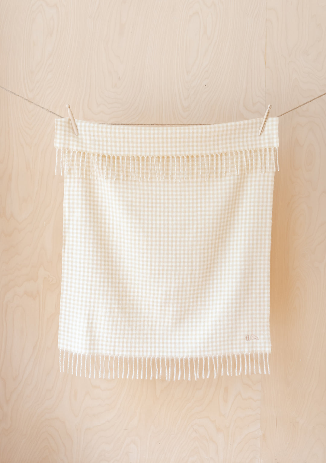 TBCo Lambswool Baby Blanket in Oatmeal Gingham hanging on clothesline, displaying fringed edges and micro check pattern