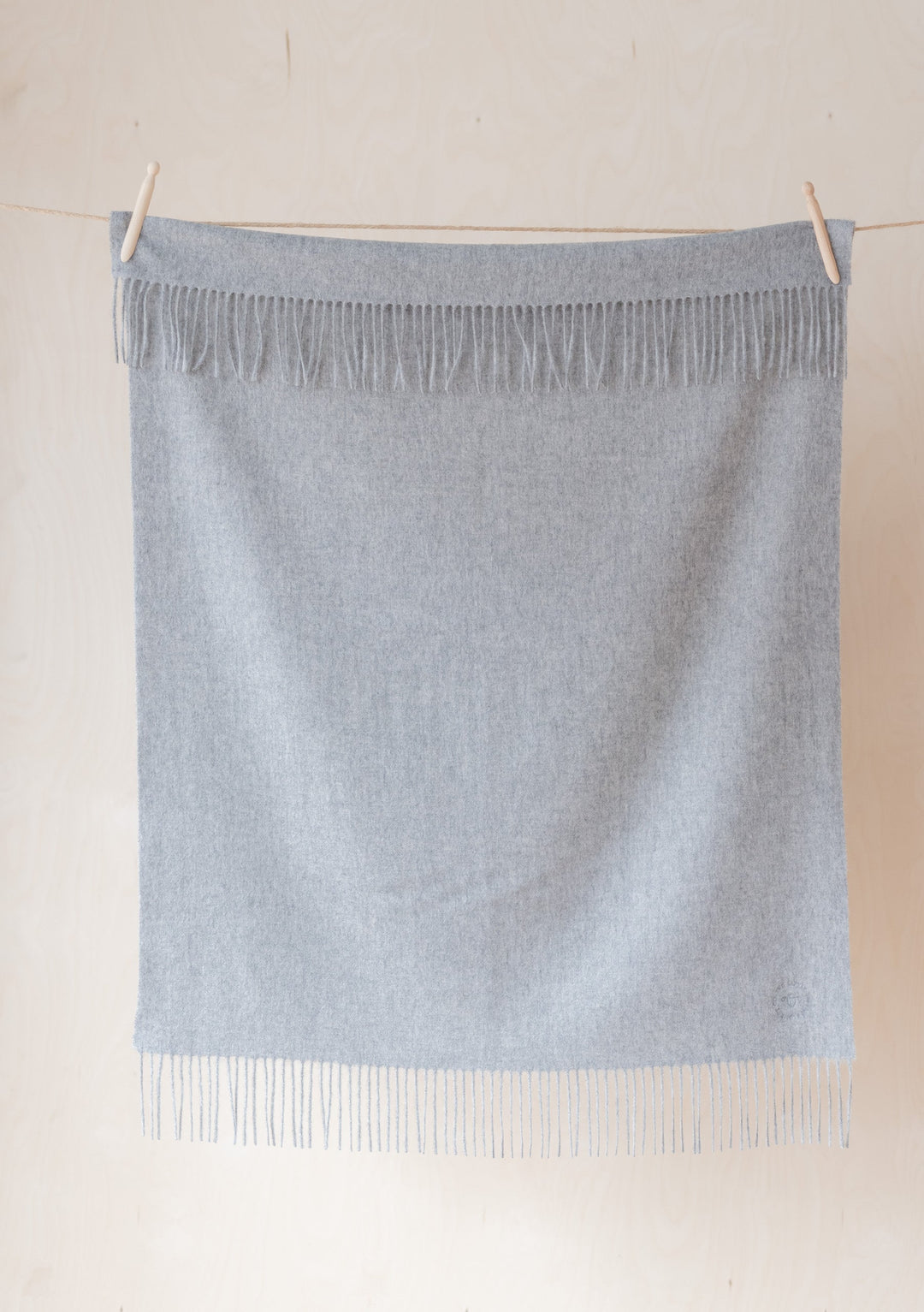 TBCo Lambswool Baby Blanket in Light Grey Melange hanging on clothesline with fringe detail, showing soft woven texture