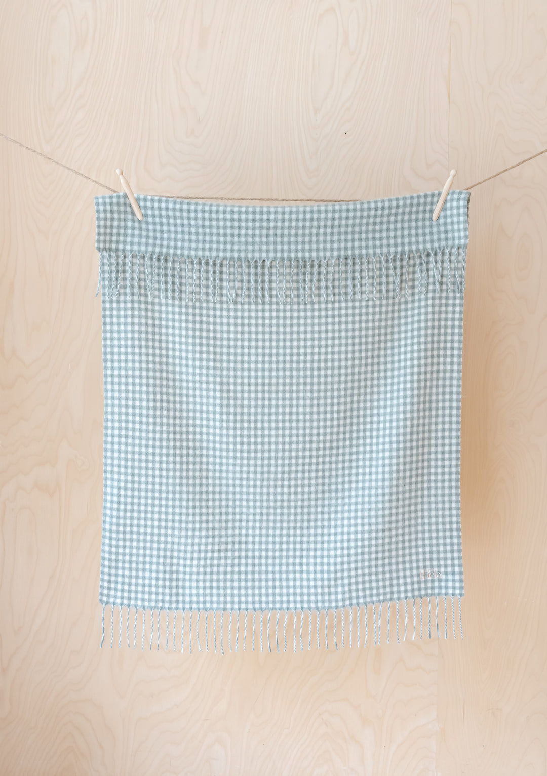 TBCo Lambswool Baby Blanket in sage and cream gingham pattern, hanging on a line showing fringed edges and soft texture