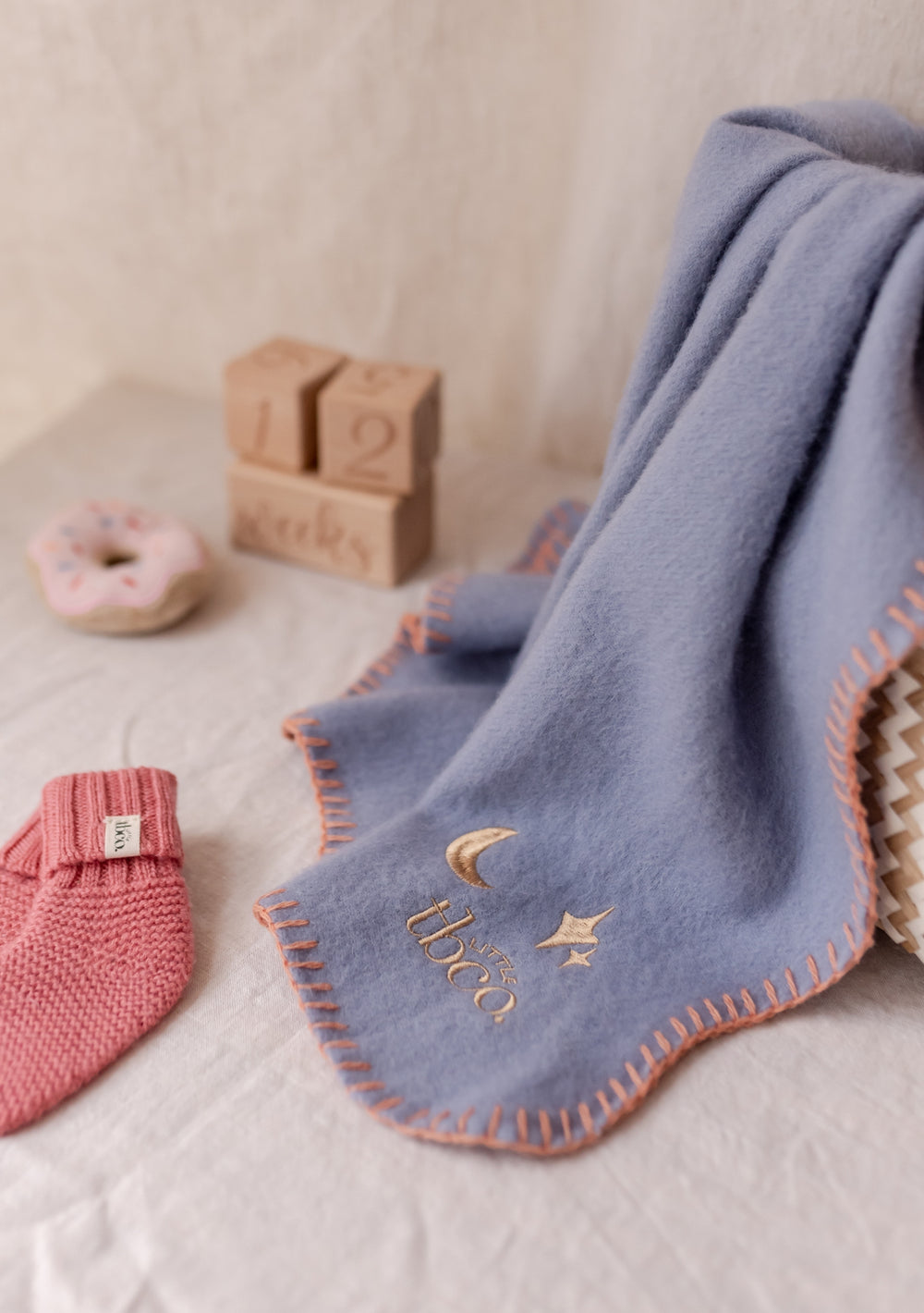 TBCo Lambswool Baby Blanket in Lilac with peach scalloped edge and embroidered moon and star detail, styled with wooden blocks