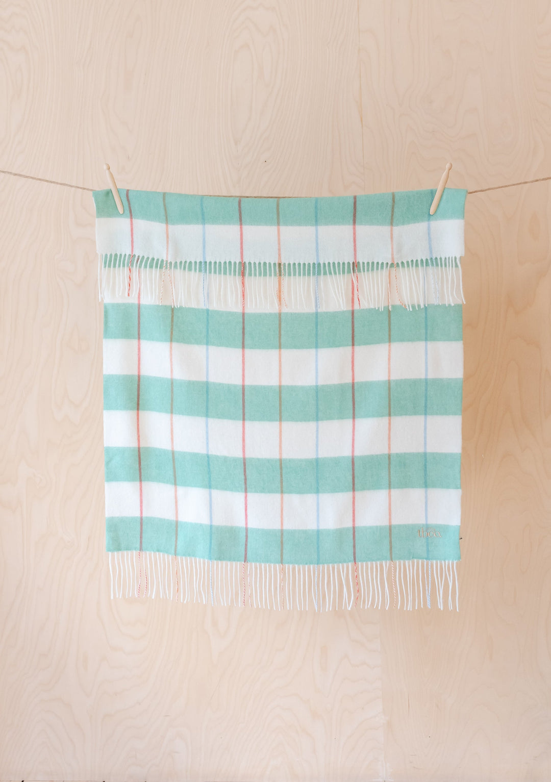 TBCo Lambswool Baby Blanket in Mint Stripe hanging on clothesline, displaying soft mint and white stripes with delicate fringe detail