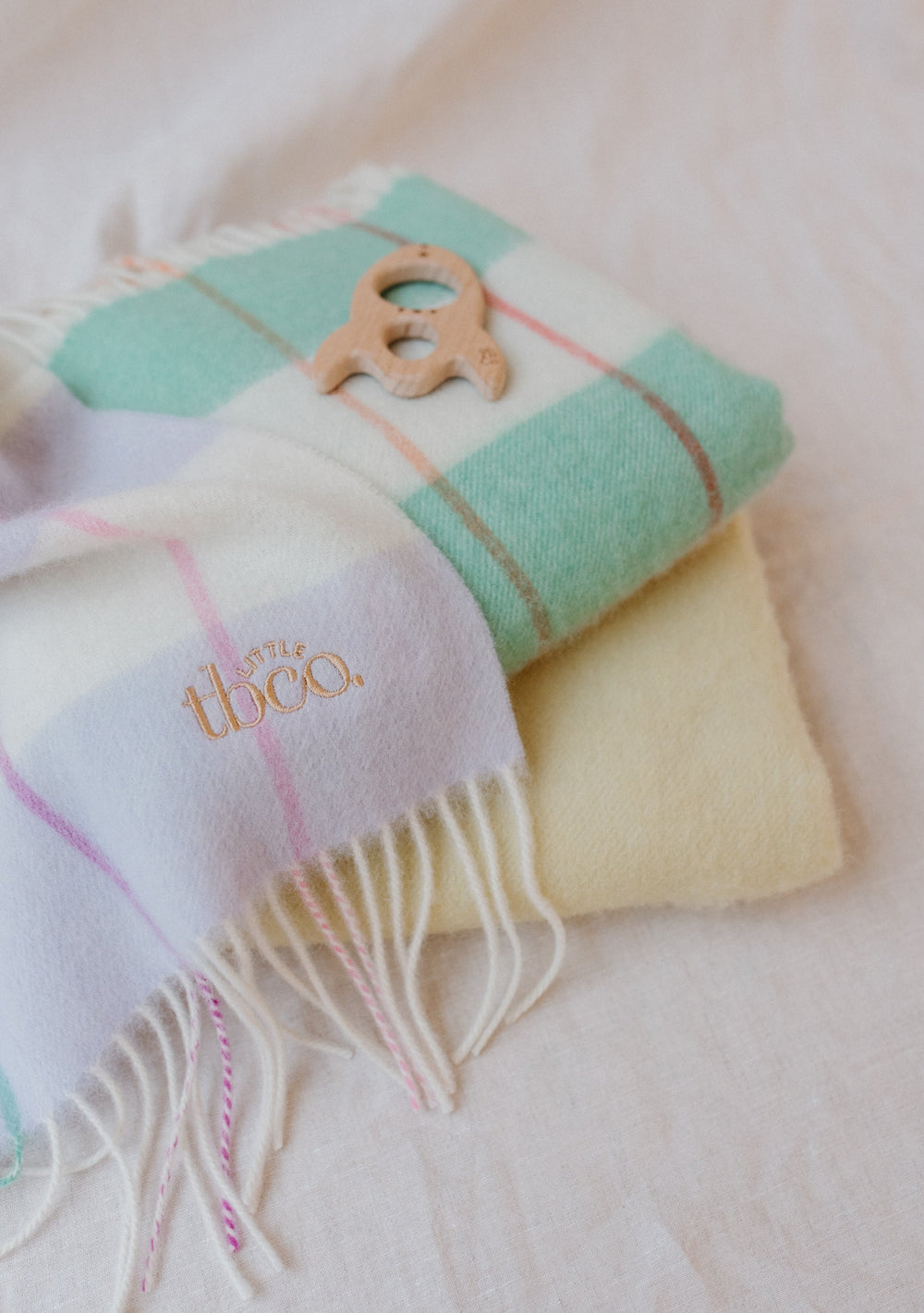 Folded TBCo Lambswool Baby Blanket in Mint Stripe with fringe detail, showing embroidered logo and pastel checkered pattern