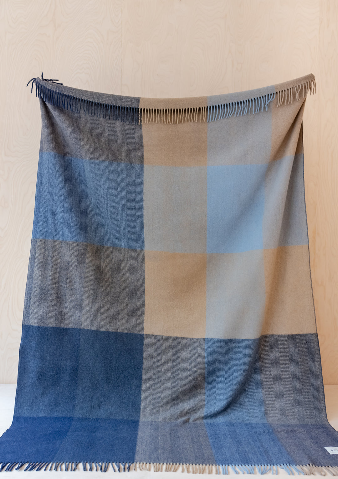 TBCo recycled wool extra large blanket featuring blue herringbone block check pattern with fringed edges on wooden backdrop