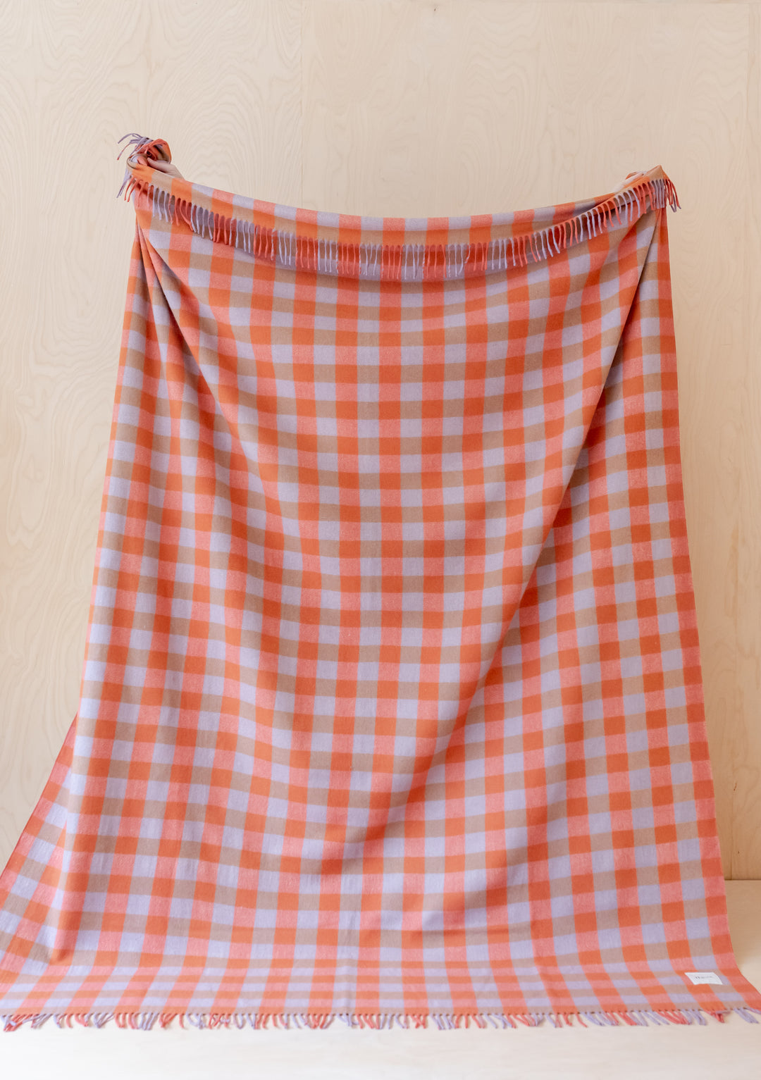 TBCo Recycled Wool Extra Large Blanket in orange and grey gingham pattern with fringed edges displayed hanging against cream wall