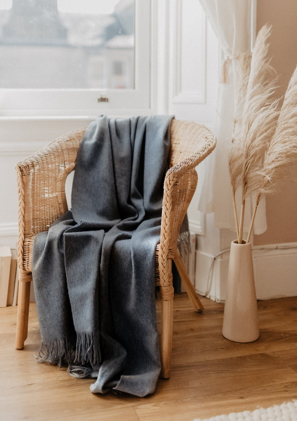 TBCo Cashmere Small Blanket in Charcoal Melange draped elegantly over rattan chair beside pampas grass in bright room