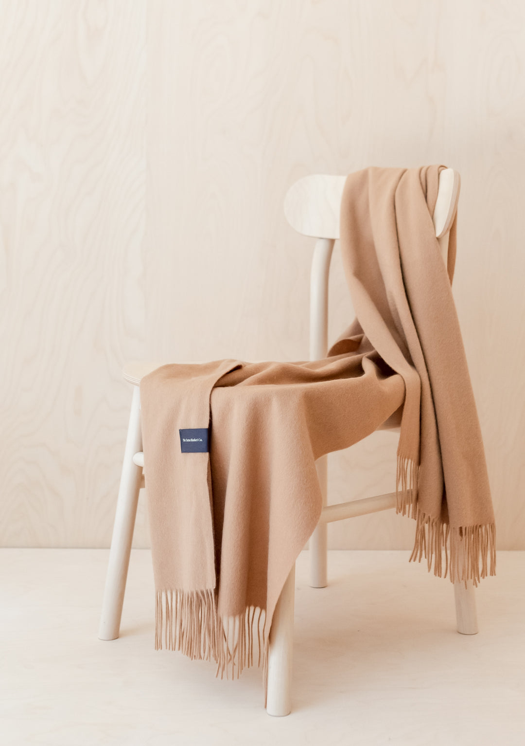 TBCo Cashmere Small Blanket in Camel draped elegantly over white chair, showcasing fringed edges and luxurious texture