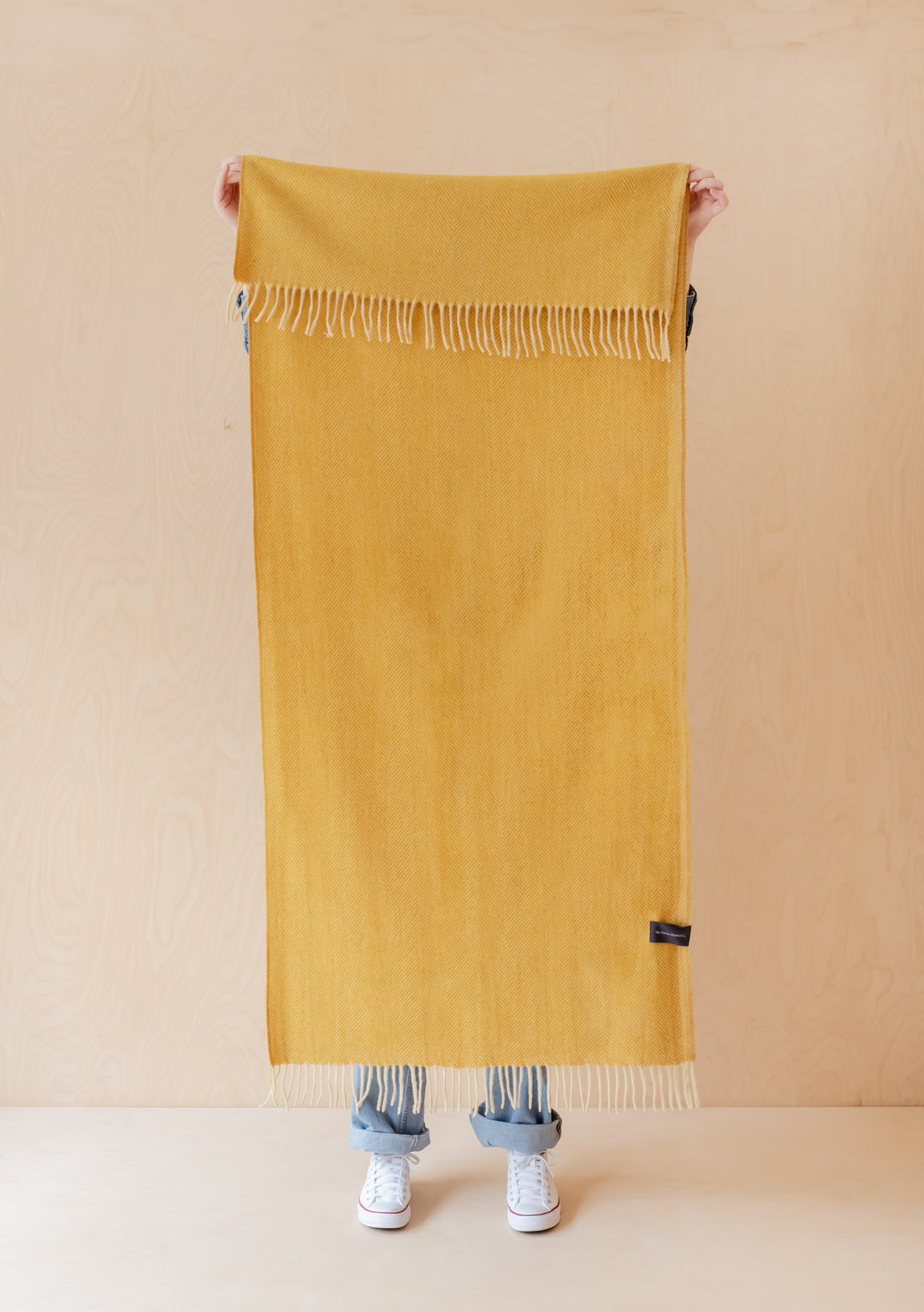 TBCo Recycled Wool Kids Blanket in mustard herringbone pattern displayed with fringed edges, showing full length and texture