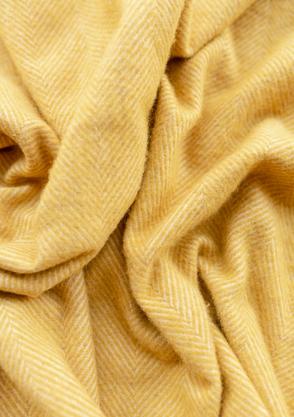 Close-up of TBCo recycled wool kids blanket in mustard herringbone pattern showing textured weave and soft draping folds