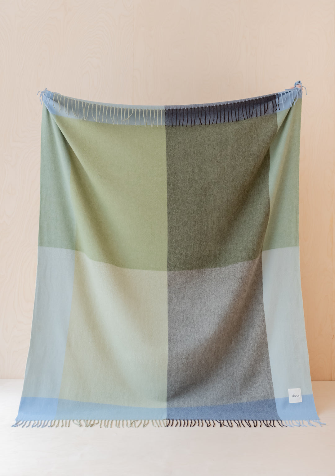 TBCo Lambswool Blanket in Green Frame Check displayed flat, showing soft geometric pattern in sage green and grey tones with fringe