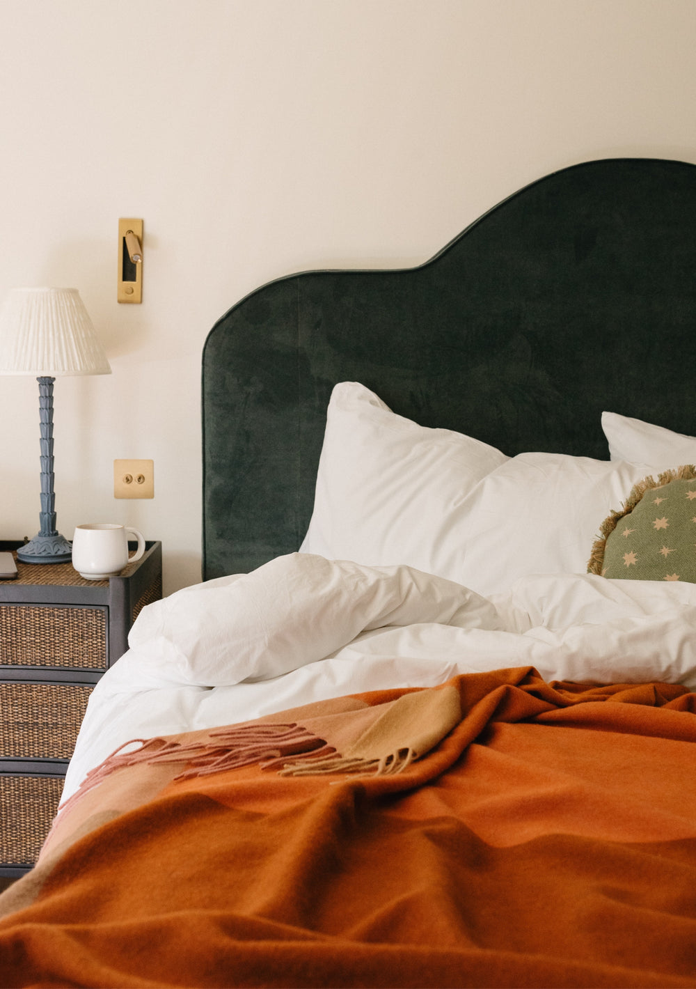 TBCo Lambswool Blanket in Rust Frame Check draped over white bedding against dark green velvet headboard with table lamp