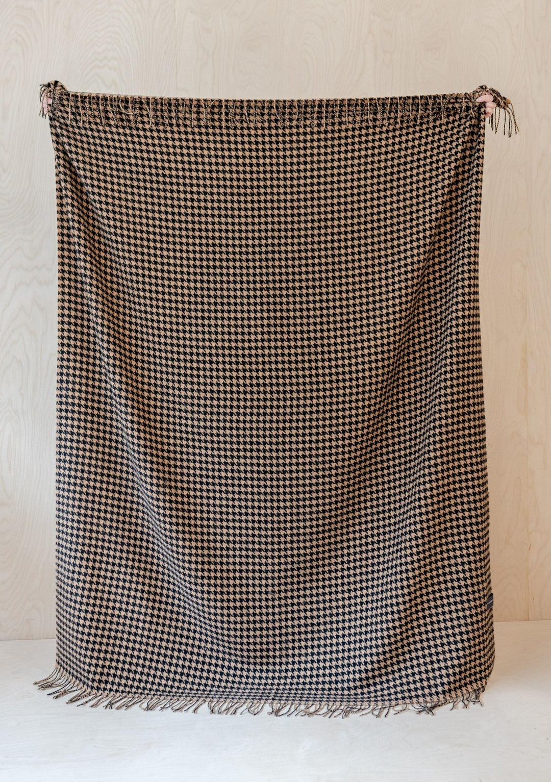 TBCo Lambswool Blanket in Camel Houndstooth pattern with fringed edges, displayed flat against light wooden background