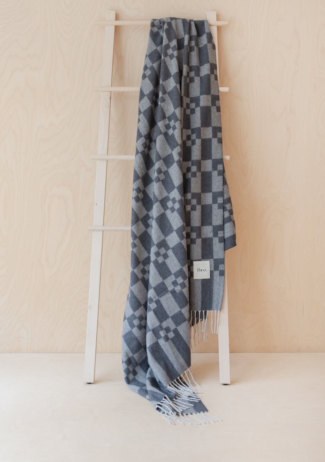 TBCo Grey Geometric Block Cashmere & Merino Blanket draped on wooden ladder, showcasing geometric pattern and fringe detail