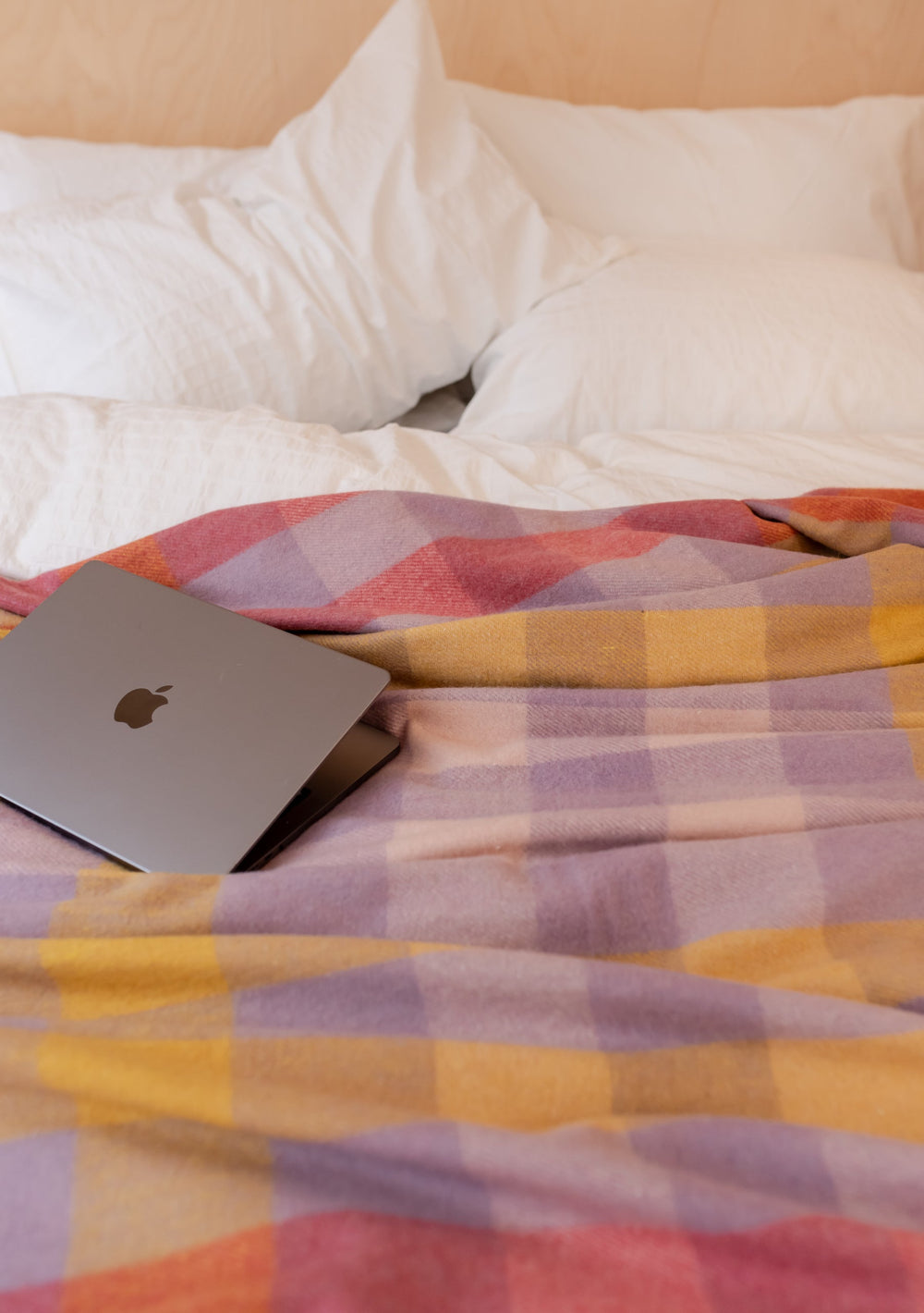 TBCo Recycled Wool Blanket in Lilac Gradient Gingham draped over white bedding with laptop, showing pastel check pattern