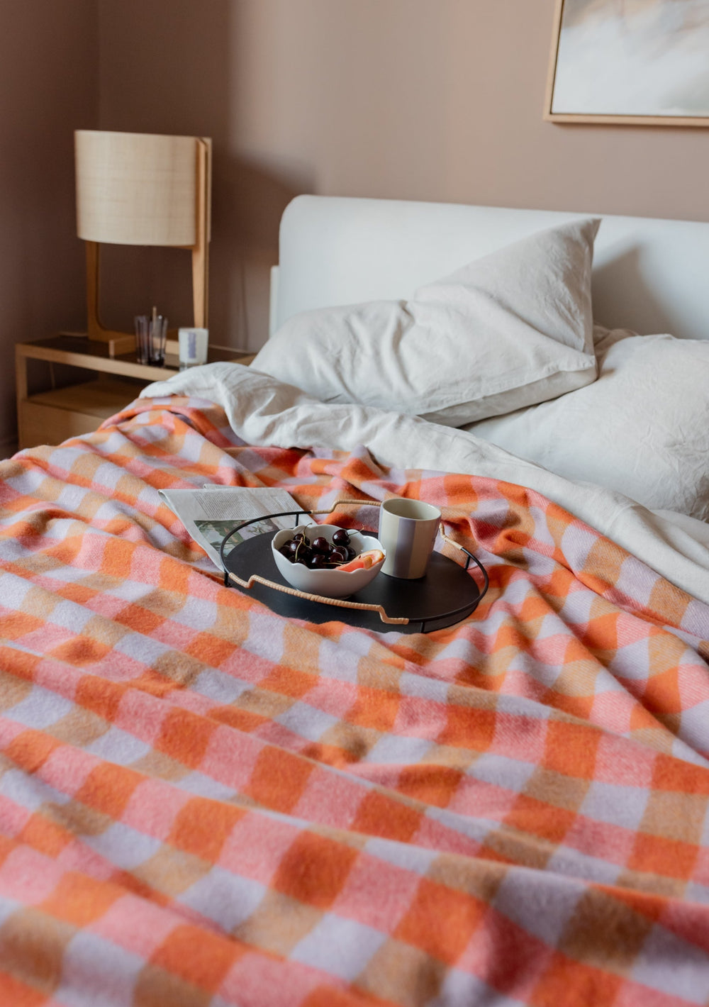 TBCo Recycled Wool Blanket in orange gingham pattern draped over white bedding with breakfast tray and morning light