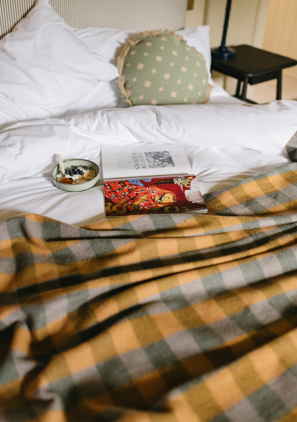 TBCo Recycled Wool Blanket in Sage Gingham draped over white bedding with book and breakfast tray, showing cosy comfort