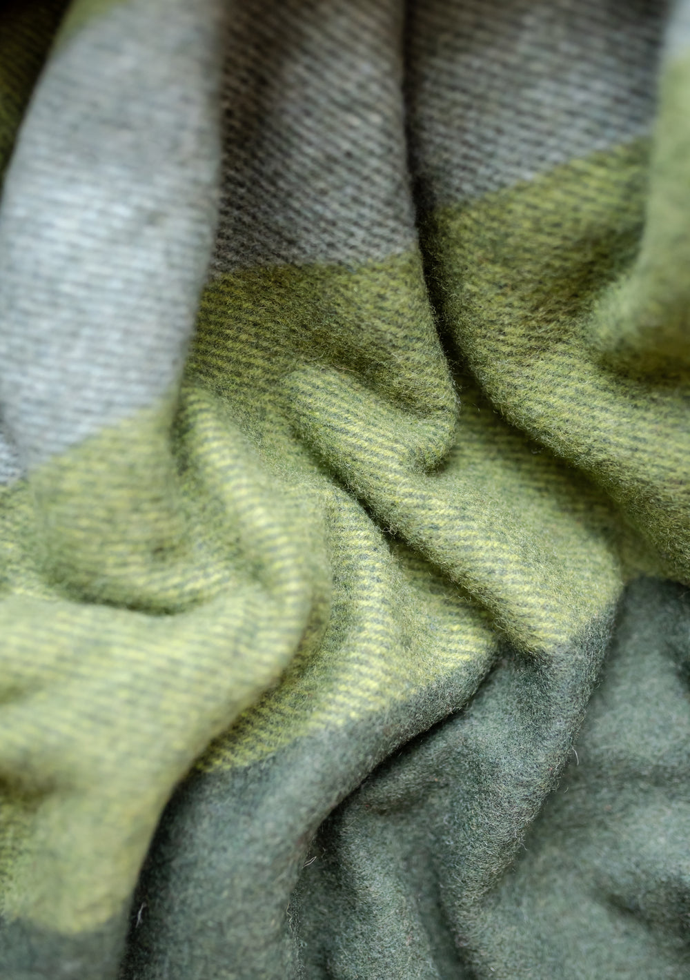 Close-up detail of TBCo recycled wool blanket in olive and grey patchwork check showing textured weave pattern